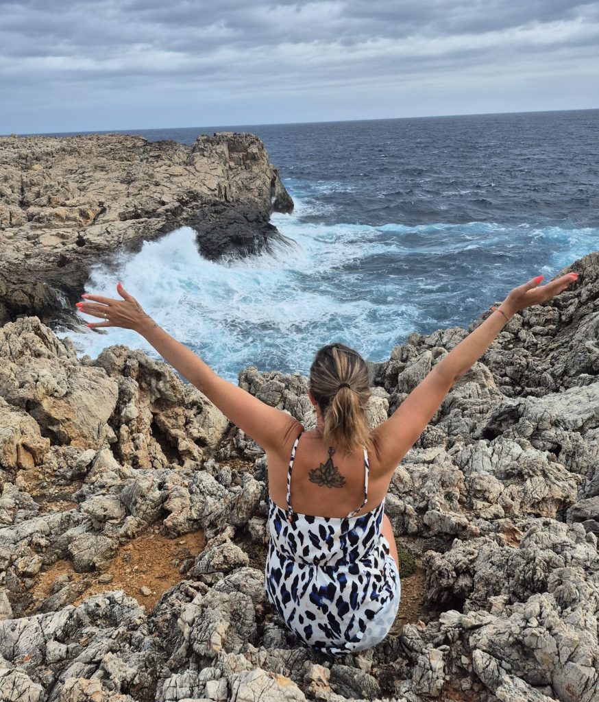 Laurence Rey face à l’immensité de la mer, assise sur les falaises, les bras ouverts vers le ciel, exprimant la liberté.