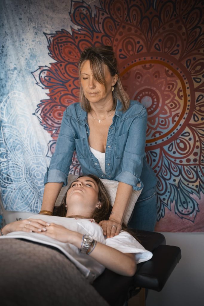 Laurence Rey en séance énergétique, les mains posées sur une patiente allongée sur le dos, les yeux fermés.
