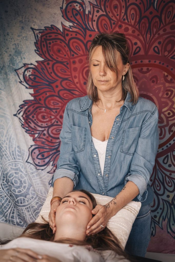 Laurence Rey en séance énergétique, les mains posées sur une patiente allongée sur le dos, les yeux fermés.